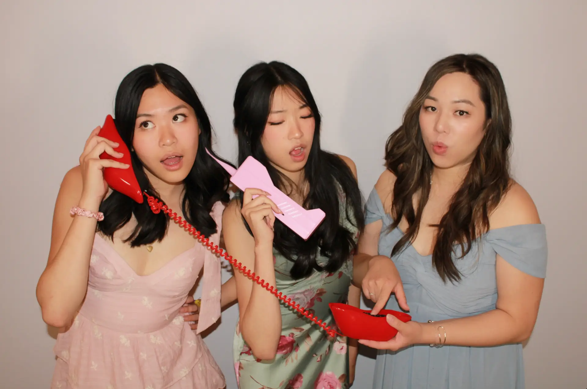 Three guests posing playfully with retro telephone props at the Mona's Booth photo booth