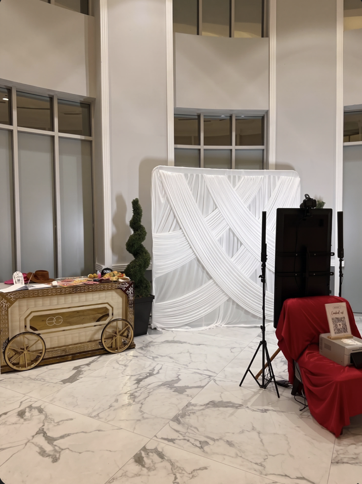 Mirror photo booth with a white draped backdrop and red-draped print station in a marble venue lobby