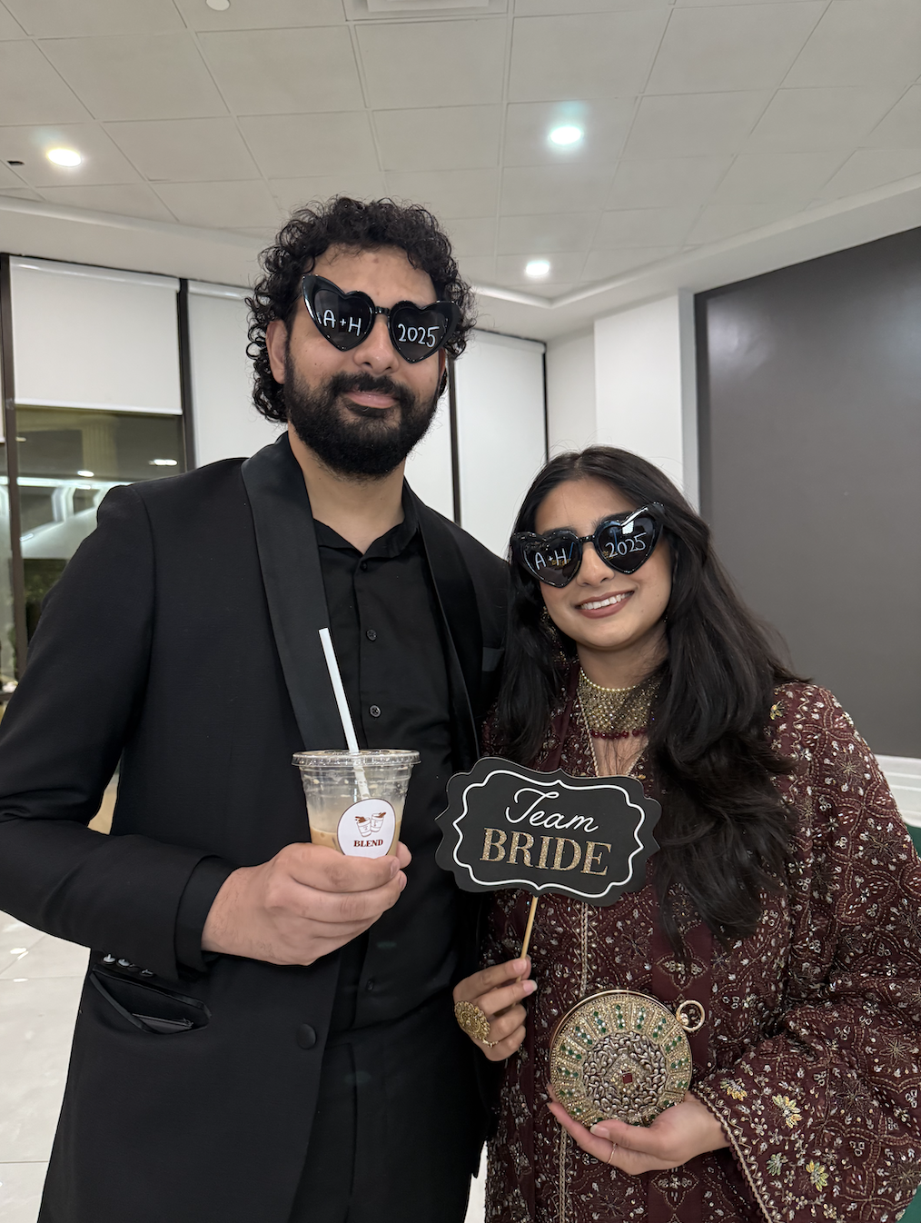 Couple in heart-shaped A+H 2025 sunglasses holding a Team Bride sign