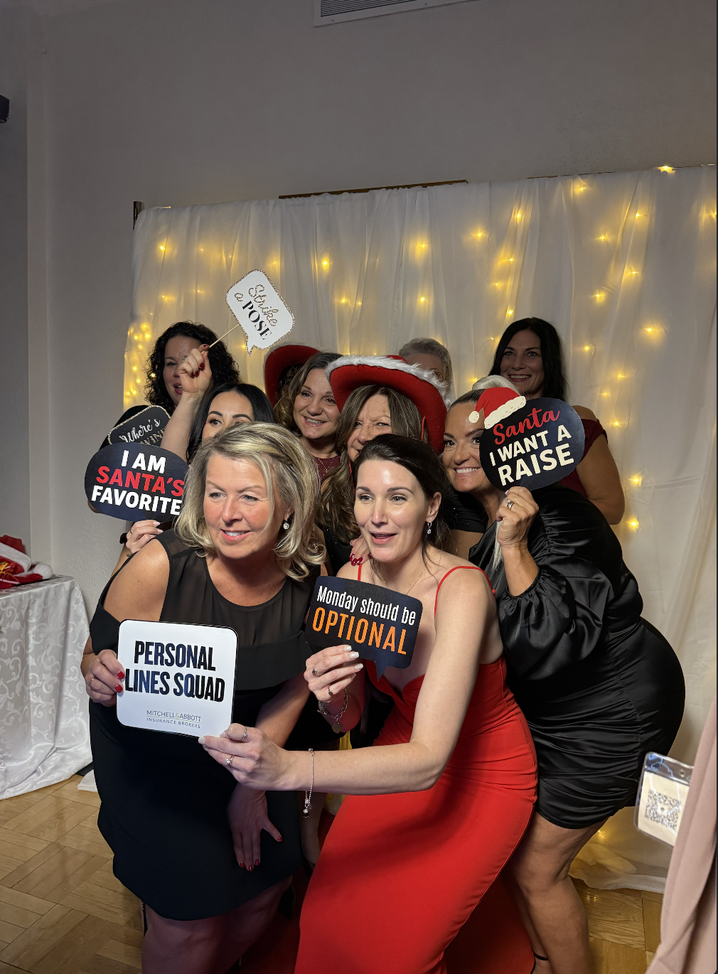 Group of guests posing with holiday photo booth signs in front of a fairy lights backdrop