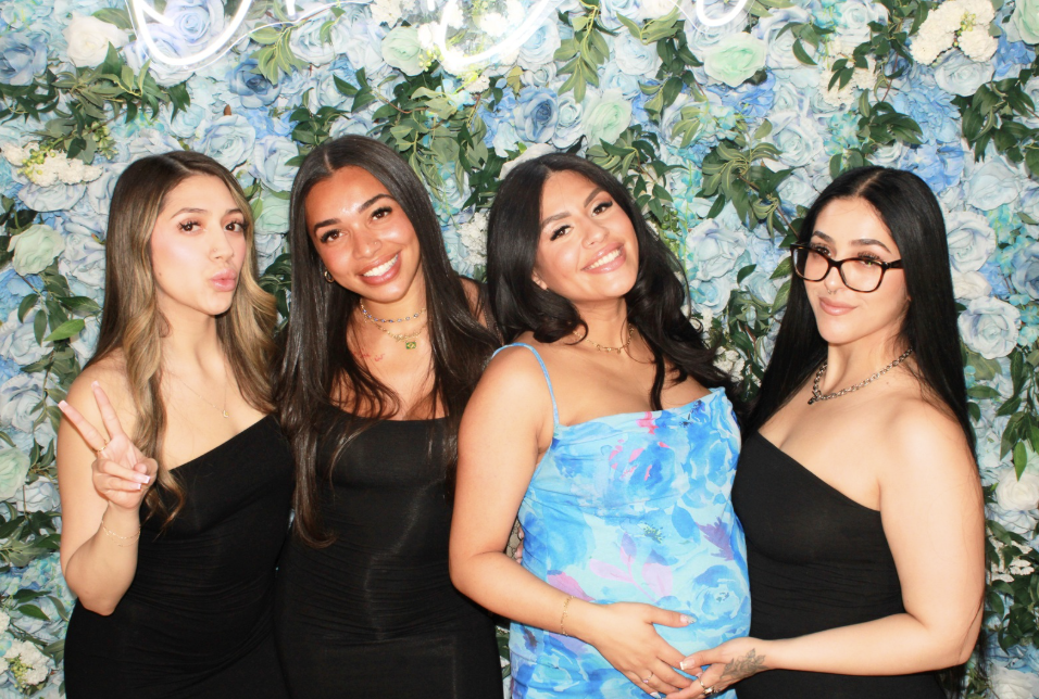 Four friends smiling in front of a blue and white flower wall at the Mona's Booth photo booth in Toronto