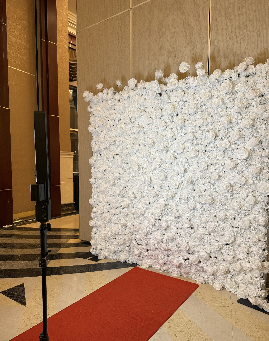 White rose flower wall backdrop with a red carpet beside the Mona's Booth mirror photo booth